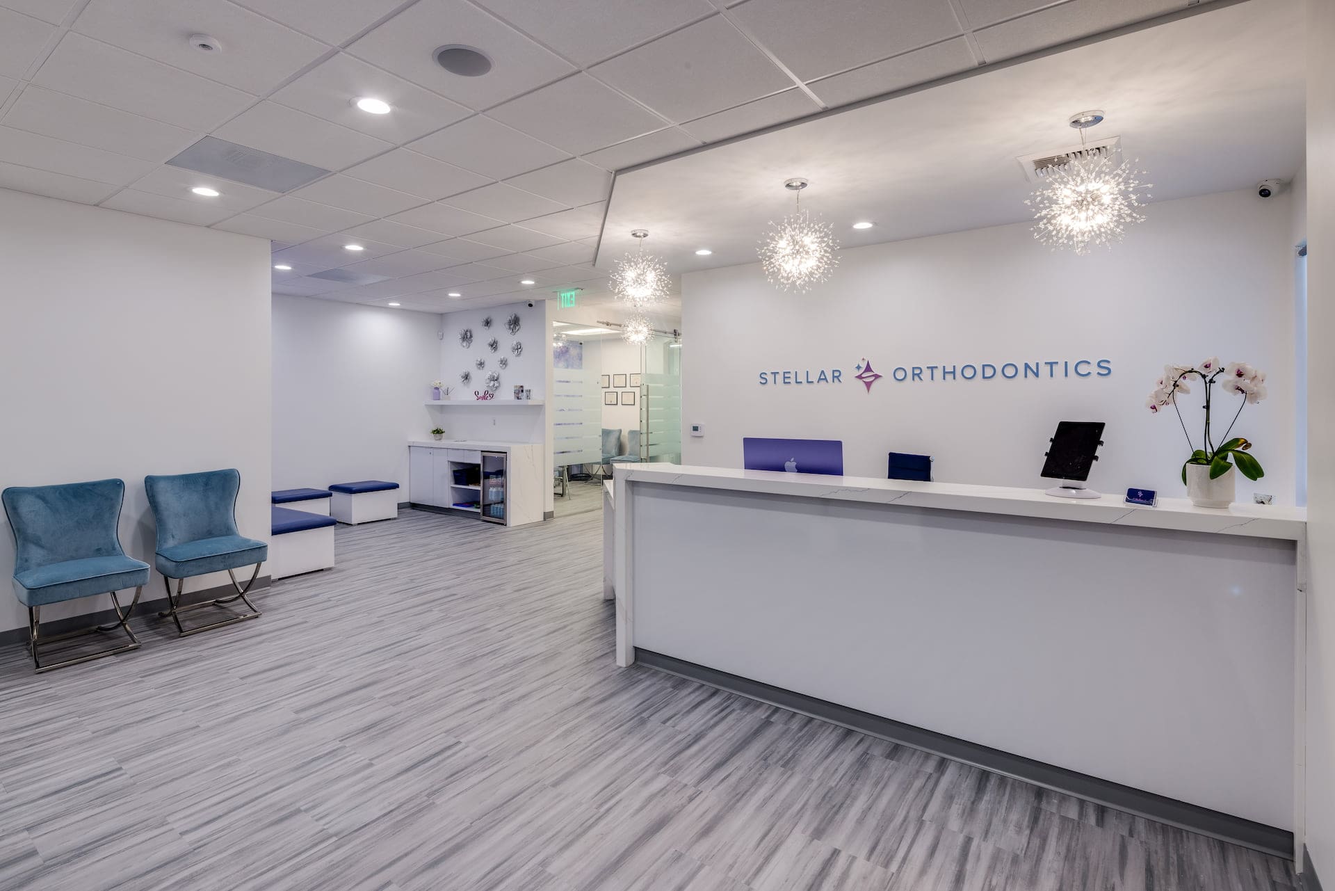 The office of Stellar Orthodontics in San Marcos, CA features a modern reception desk, white decor, blue chairs in the waiting area, and a "Stellar Orthodontics" sign displayed on the wall.
