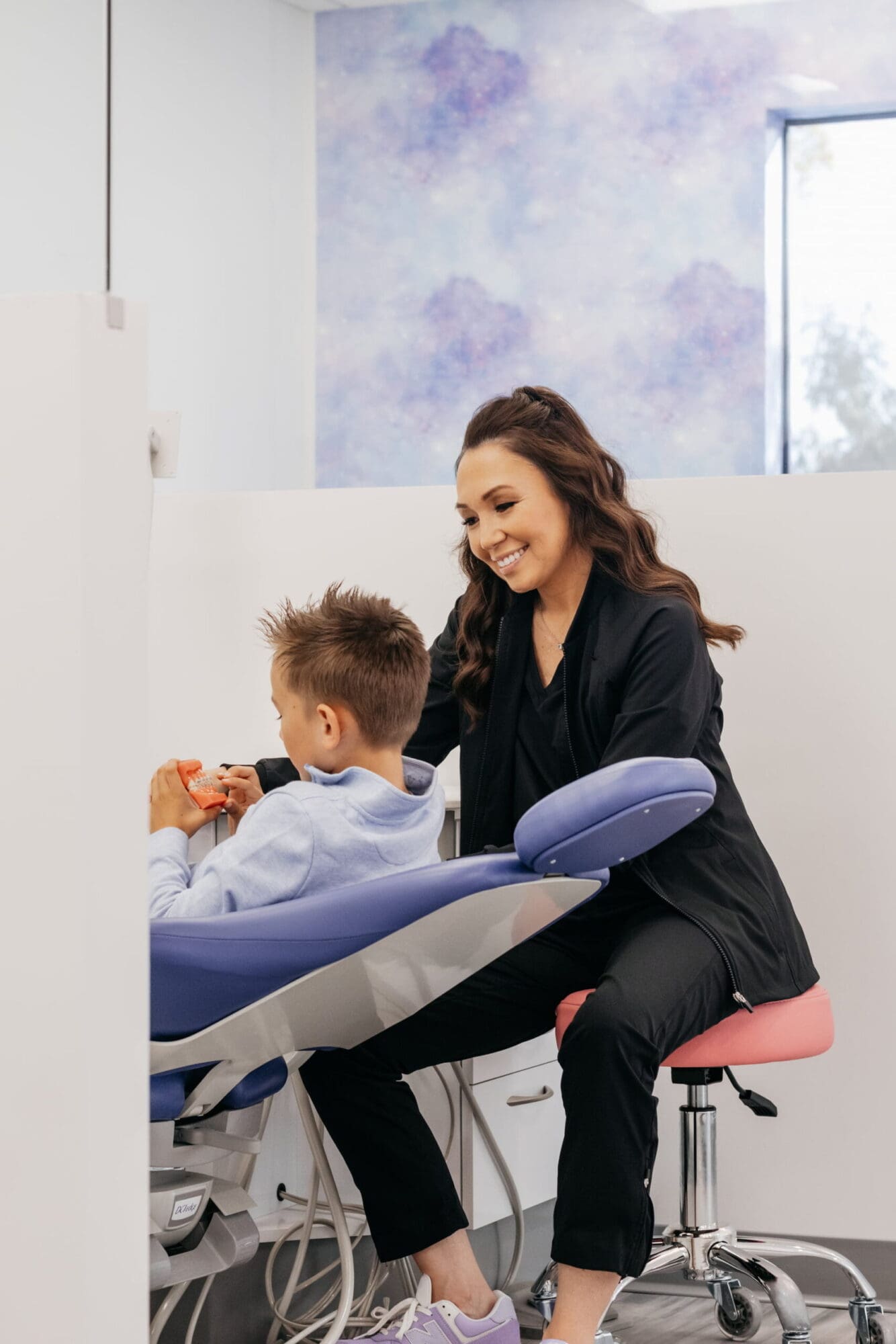 At Stellar Orthodontics in San Marcos, CA, Dr. Laura Deyo examines a boy with braces, seated and smiling in a dental chair.