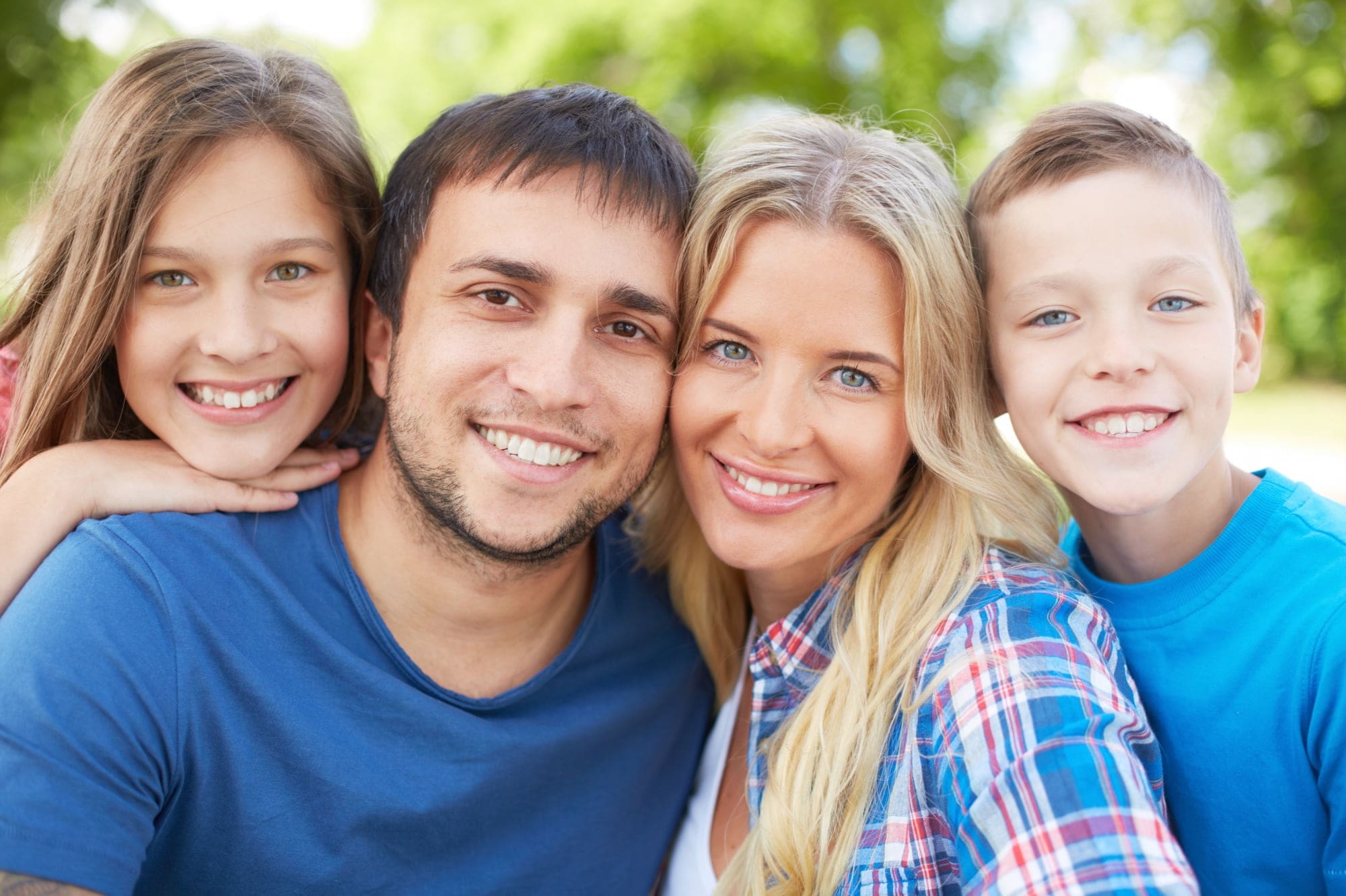 A man and woman smile with a boy and girl outdoors, all facing the camera amidst blurred trees and greenery, representing happy families with free orthodontic consultation at Stellar Orthodontics in San Marcos, CA.