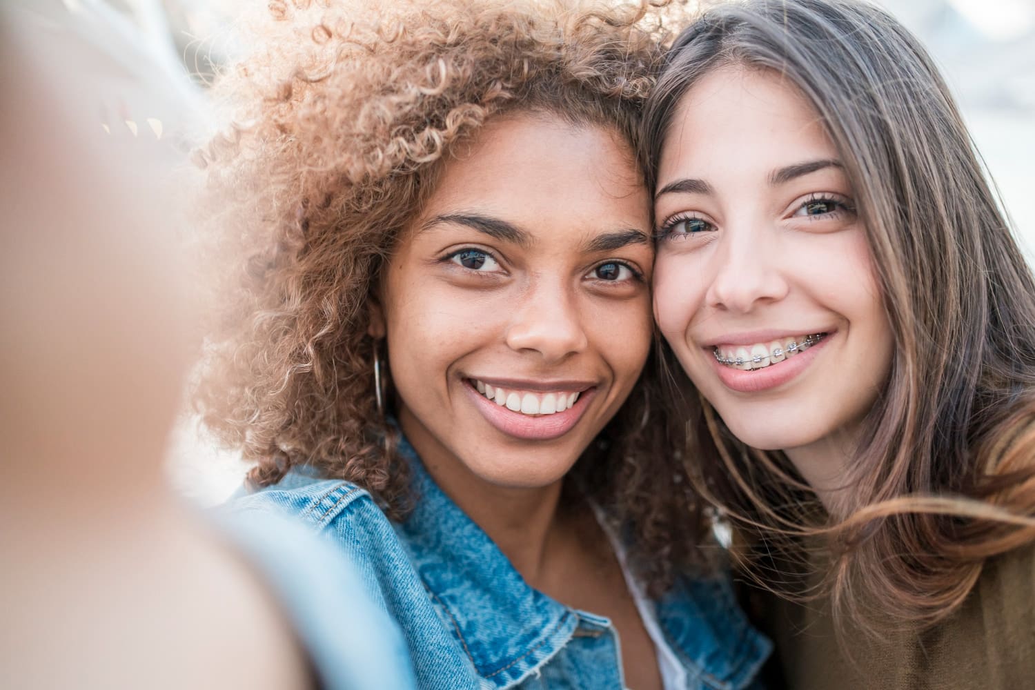 Smiling for a selfie in San Marcos, CA, two young women—one with curly hair, one with braces from Stellar Orthodontics—pose together.