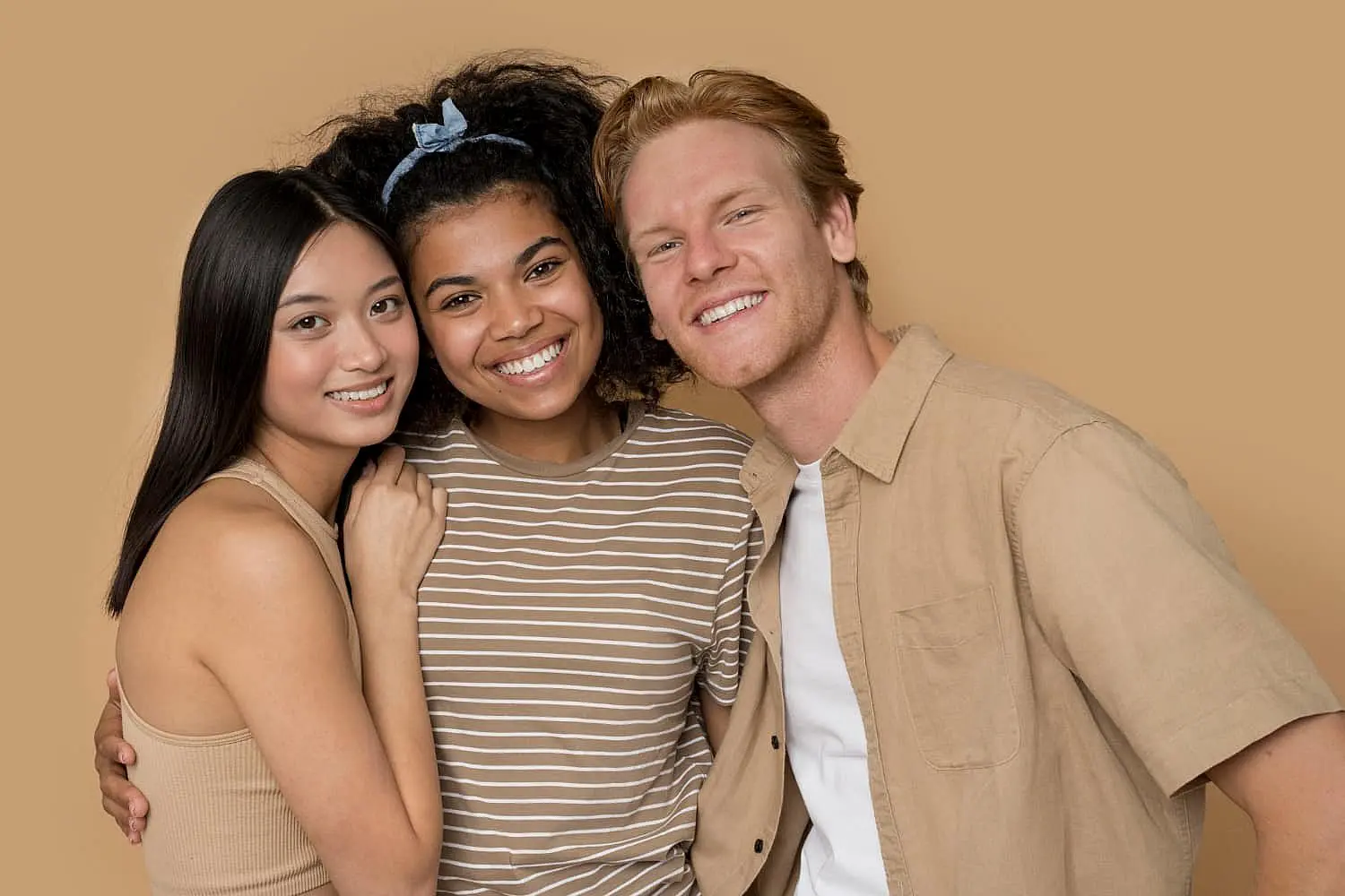 Three smiling young adults stand together against a beige background at Stellar Orthodontics in San Marcos, CA after Orthodontic Appliances treatment.