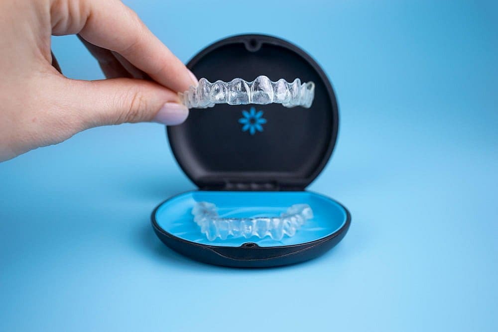 A hand displays a dental aligner Invisalign over a storage case with another aligner, for Stellar Orthodontics in San Marcos, CA.