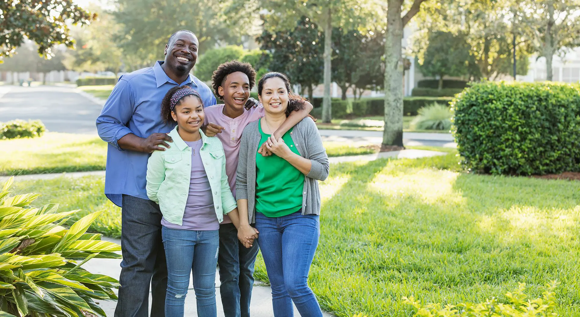 Smiling at the camera on a sunny day, a family of four stands outside in a park at Stellar Orthodontics in San Marcos, CA after undergoing Invisalign treatment.