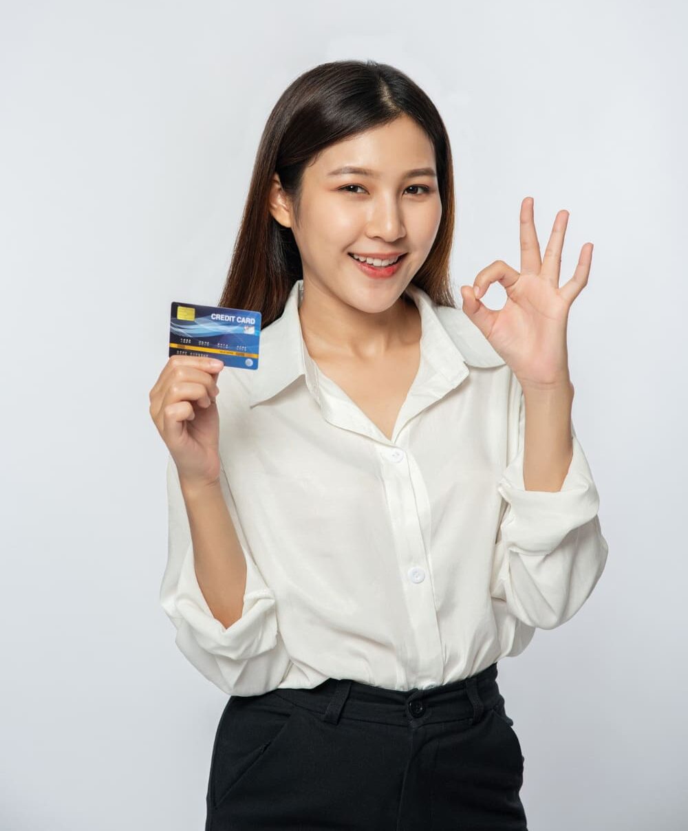 Smiling woman represent about Braces Payment Plan at Stellar Orthodontics in San Marcos, CA holds a credit card and makes an "OK" sign in a white blouse.