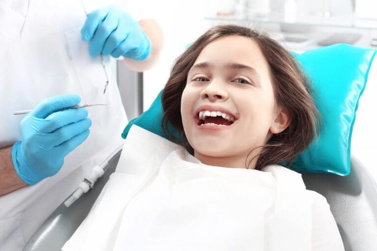 At Stellar Orthodontics in San Marcos, CA, a smiling child sits in a dental chair as a gloved dentist holds dental tools nearby - Overbite vs Underbite in San Marcos, CA.