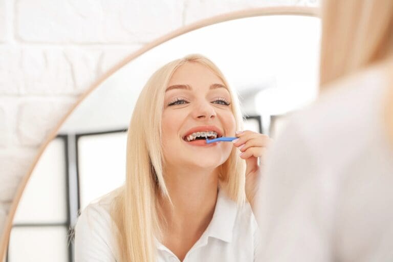 Brushing her teeth at Stellar Orthodontics in San Marcos, CA, a woman with long blonde hair looks in the mirror - How to Floss with Braces in San Marcos, CA.