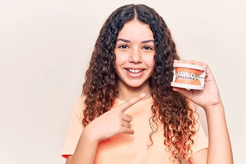 Stellar Orthodontics A smiling girl with long curly hair points to a dental model with affordable braces cost at Stellar Orthodontics in San Marcos, CA.