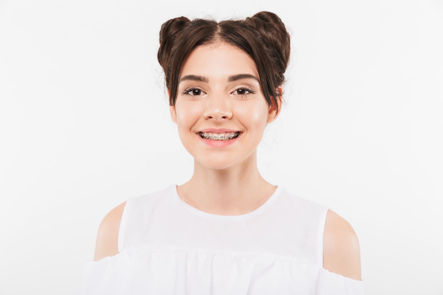 Smiling at the camera, a young woman with brown hair in two buns shows her metal braces from Stellar Orthodontics in San Marcos, CA.