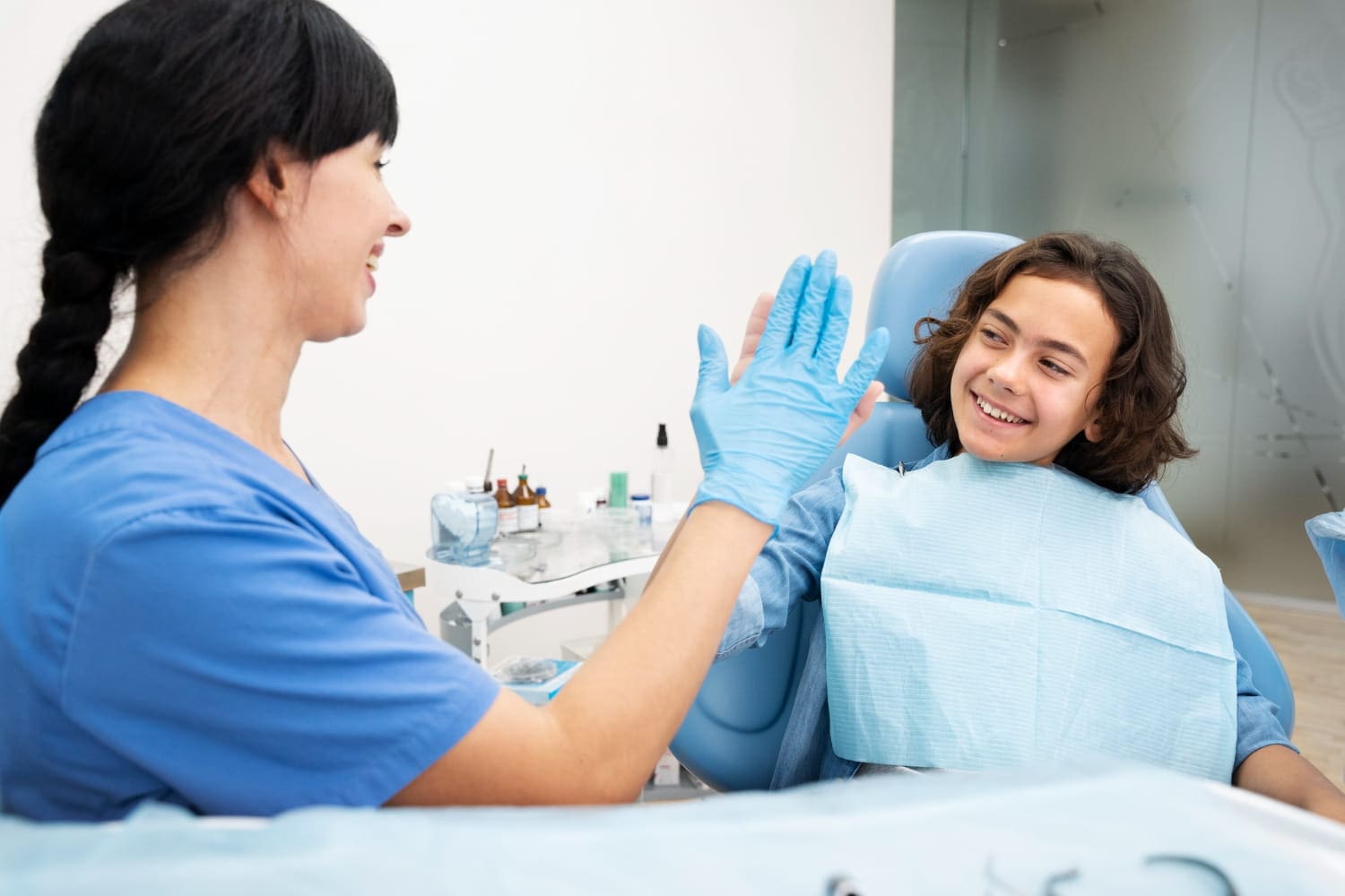 At Stellar Orthodontics in San Marcos, CA, a dentist in blue scrubs high-fives a smiling young patient with metal braces.