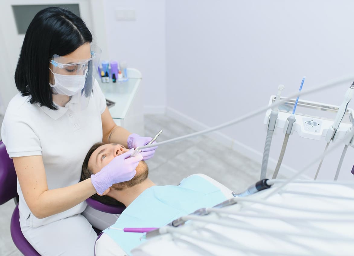 A dentist at Stellar Orthodontics in San Marcos, CA examines a patient’s metal braces while wearing a mask, gloves, and face shield.