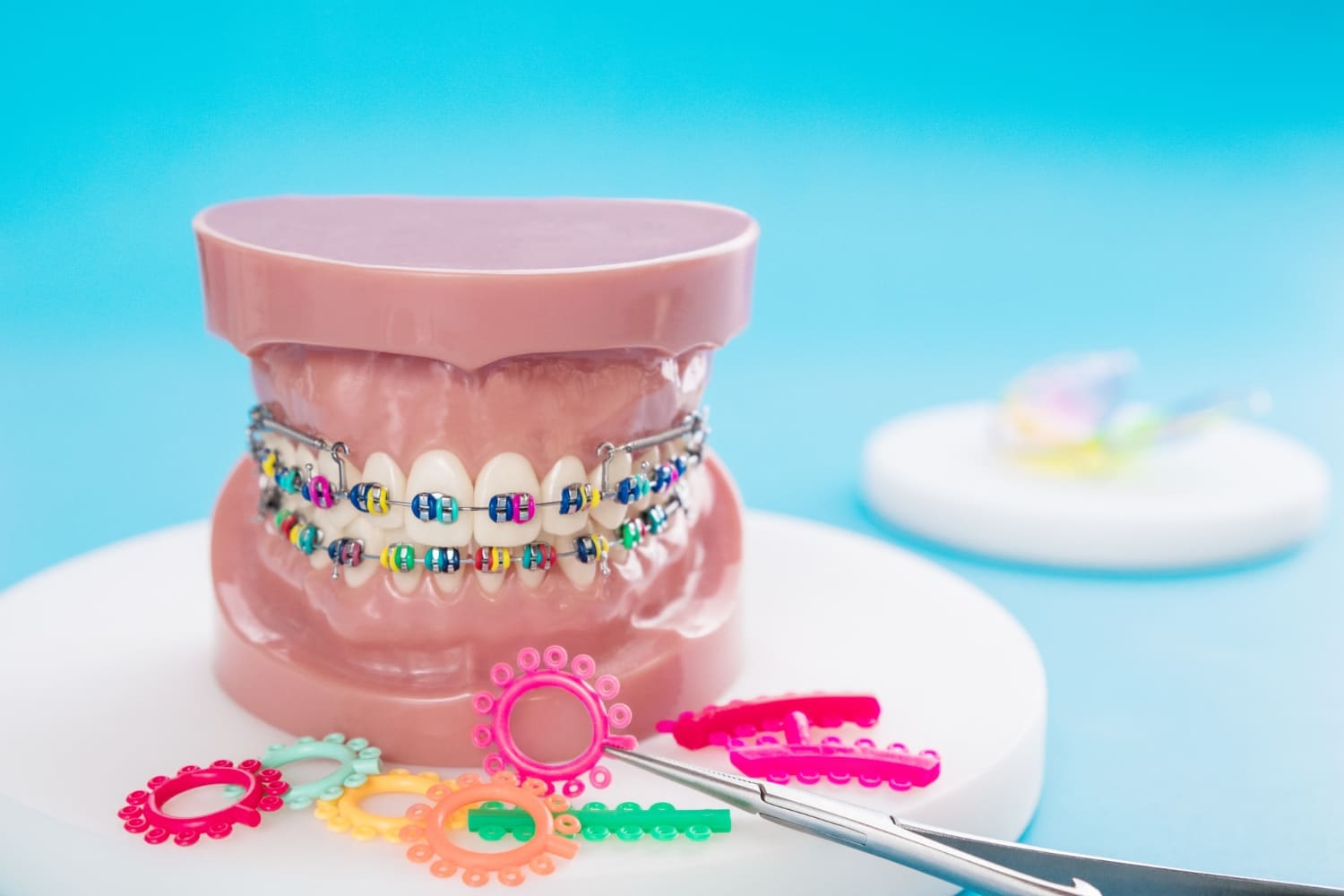 A dental model with colorful braces is displayed at Stellar Orthodontics in San Marcos, CA, surrounded by bands and tools.